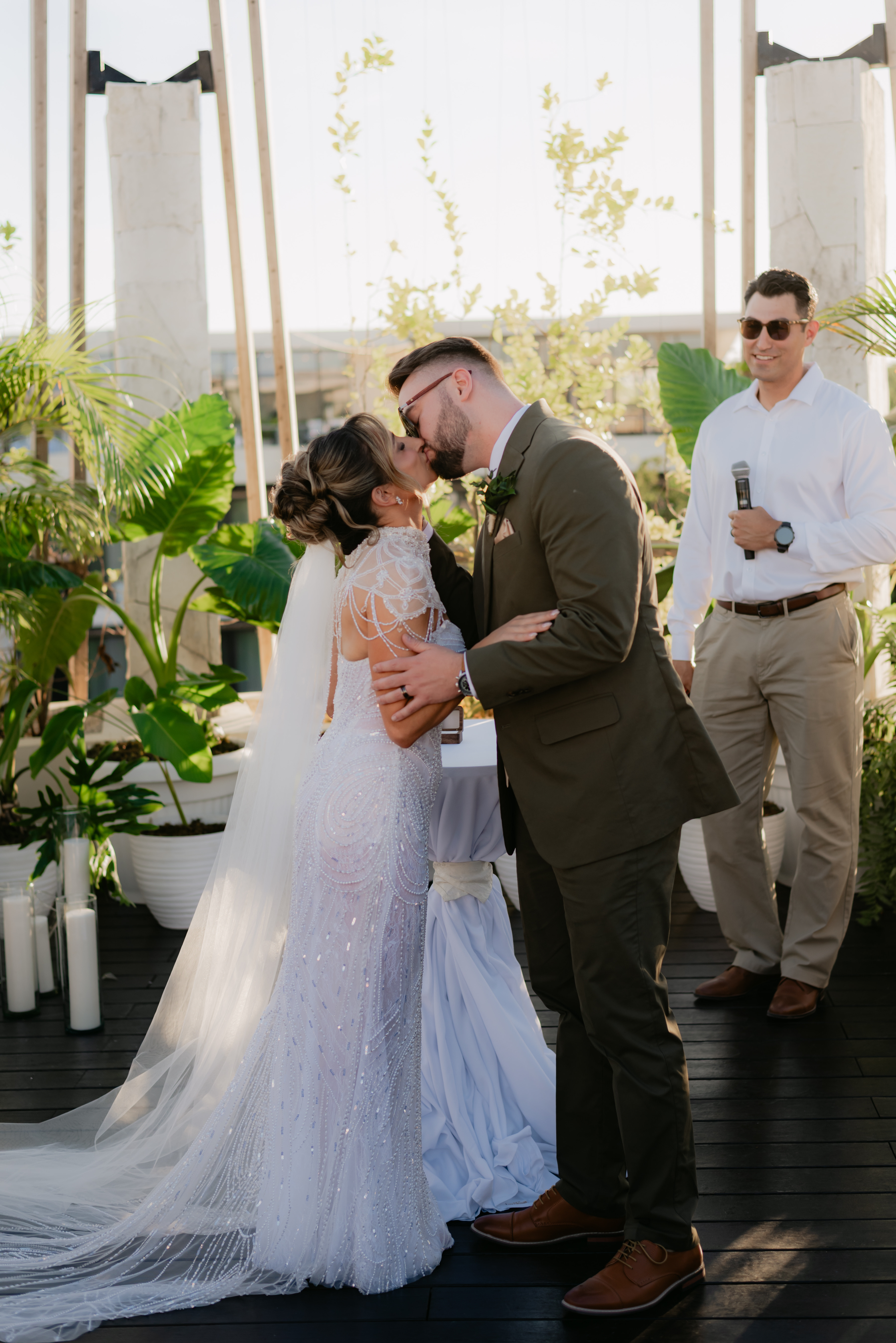 Shirley and William (Copy) share a kiss at their outdoor wedding as the officiant looks on.