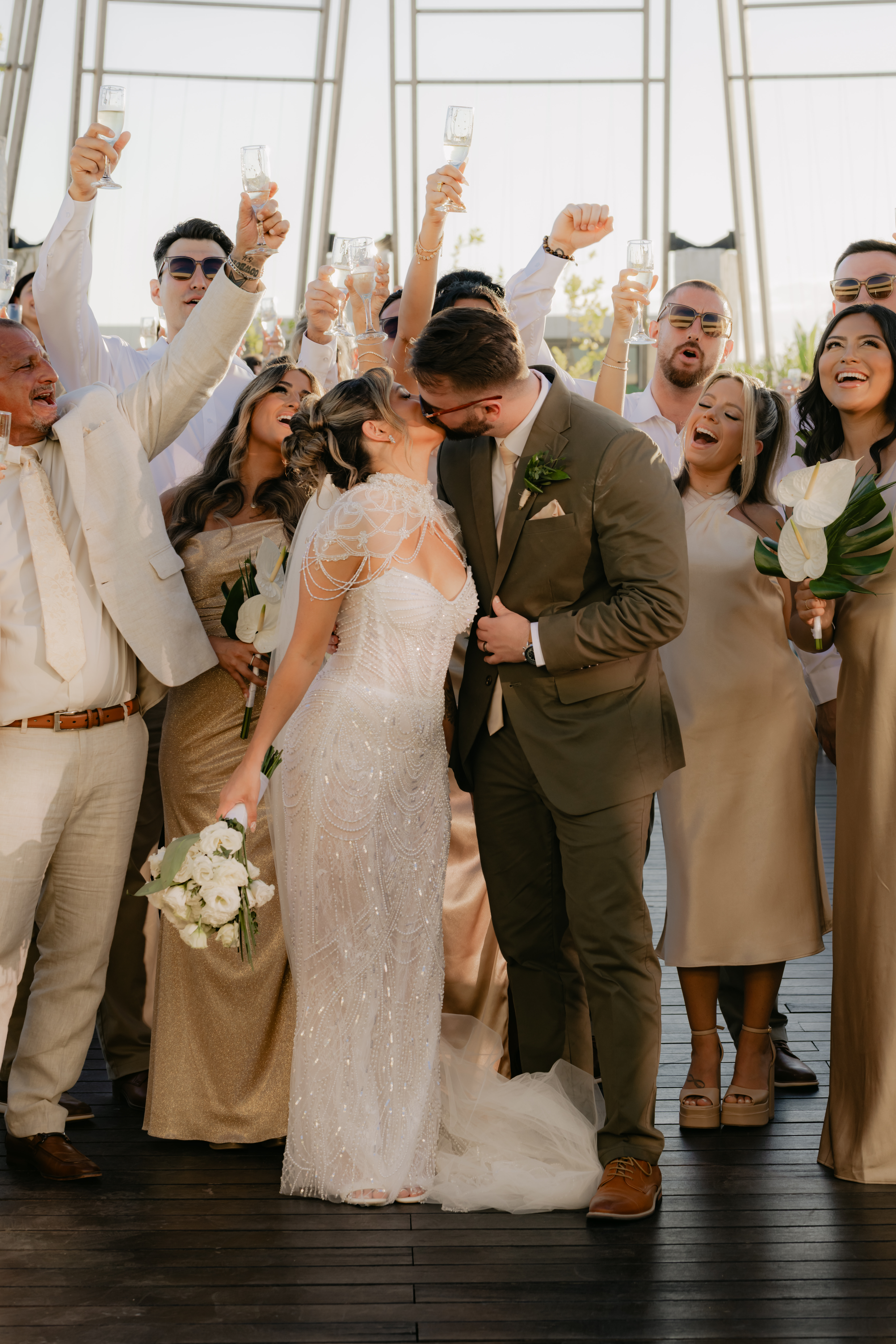 Shirley and William kiss at their destination wedding as the party in gold attire pops champagne.
