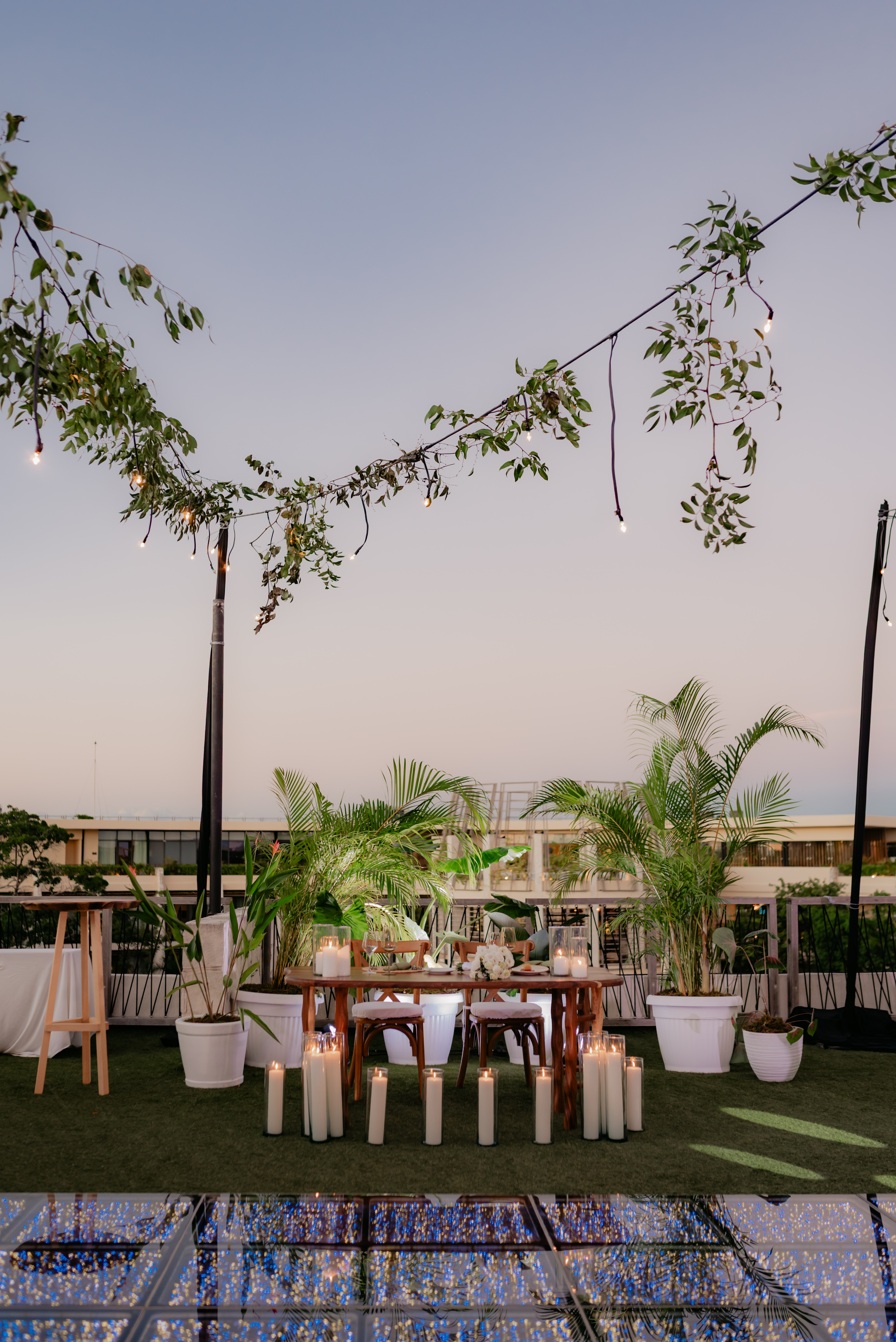 Shirley and William's destination wedding table with plants, candles, and string lights at dusk.