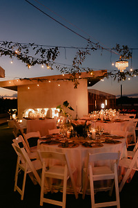 Round tables with white chairs set for dinner under string lights at a destination wedding.