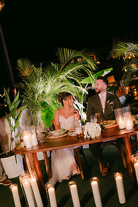 Shirley and William enjoy a nighttime destination wedding dinner at a decorated table with candles and plants.