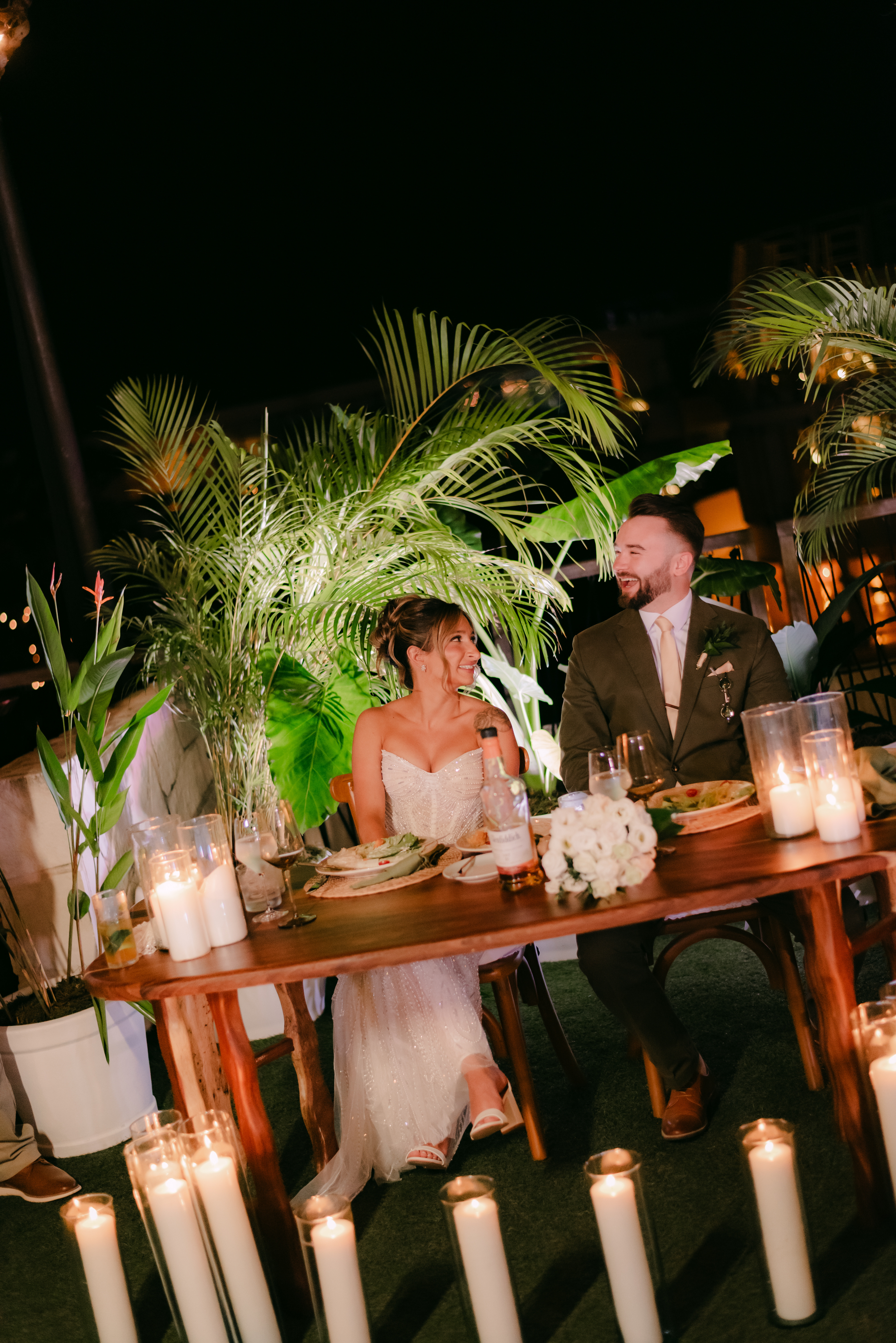 Shirley and William enjoy a nighttime destination wedding dinner at a decorated table with candles and plants.