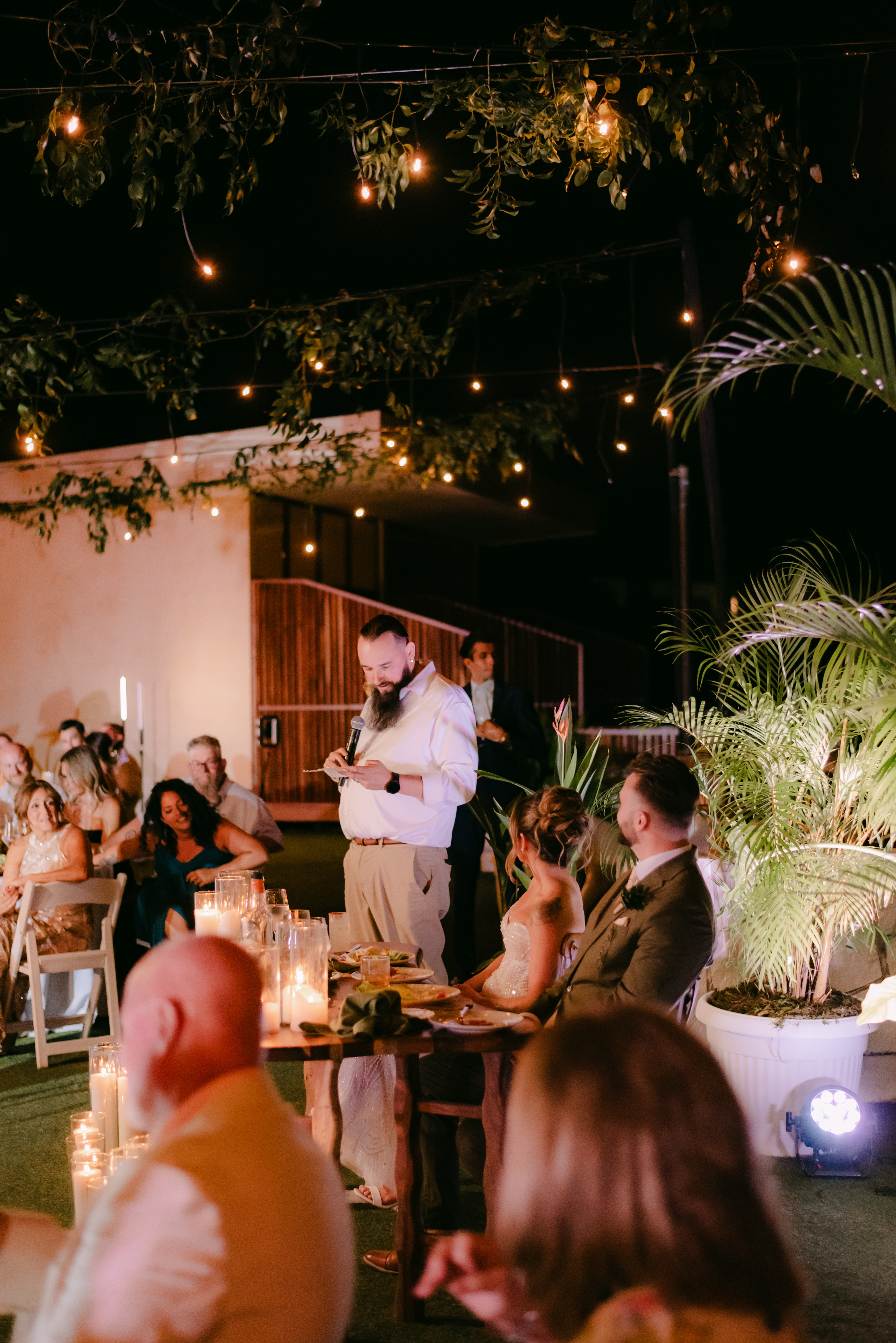 Man giving a speech at Shirley and William's destination wedding, outdoors in the evening with guests seated.
