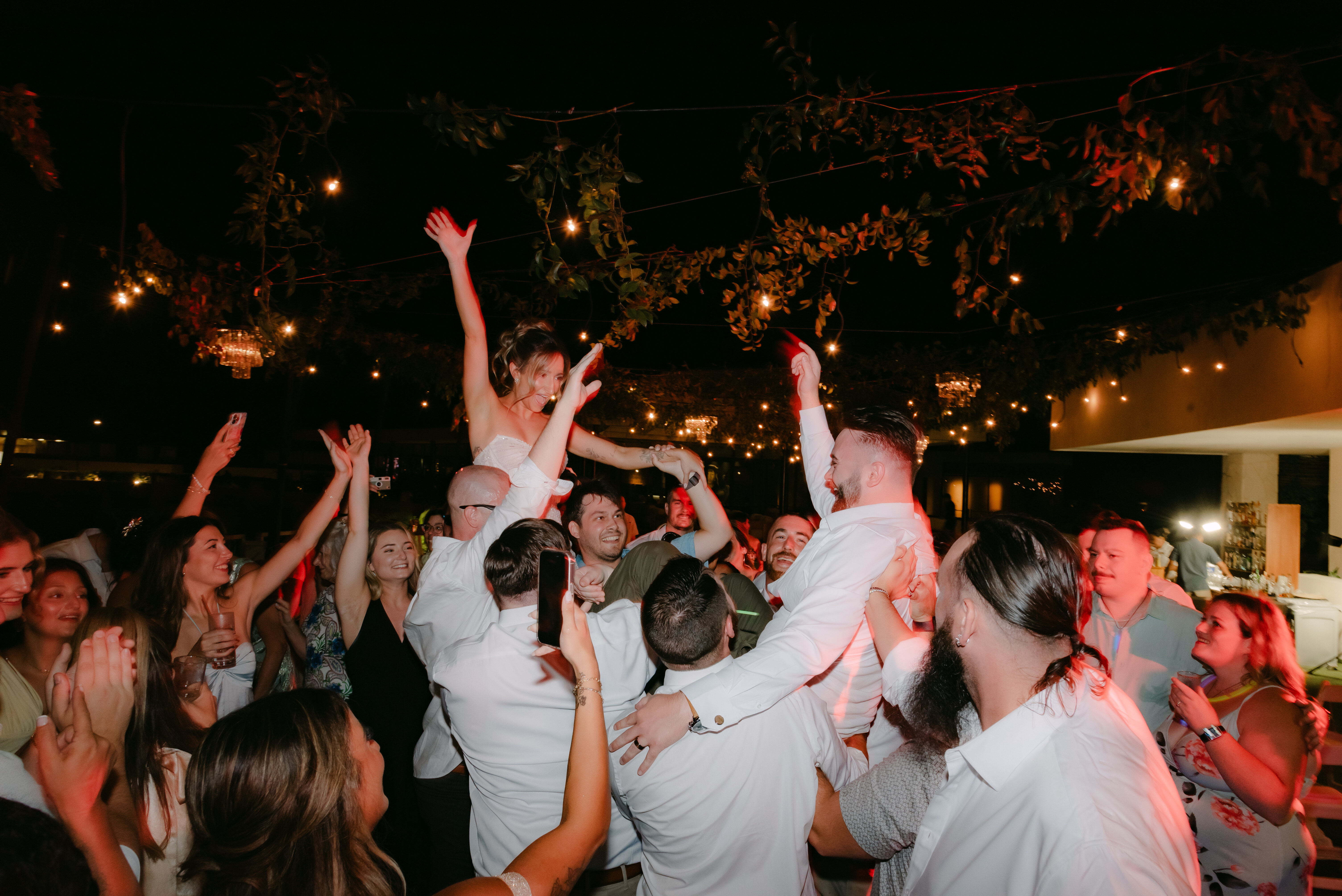 Shirley and William are lifted by guests during a festive nighttime destination wedding celebration.