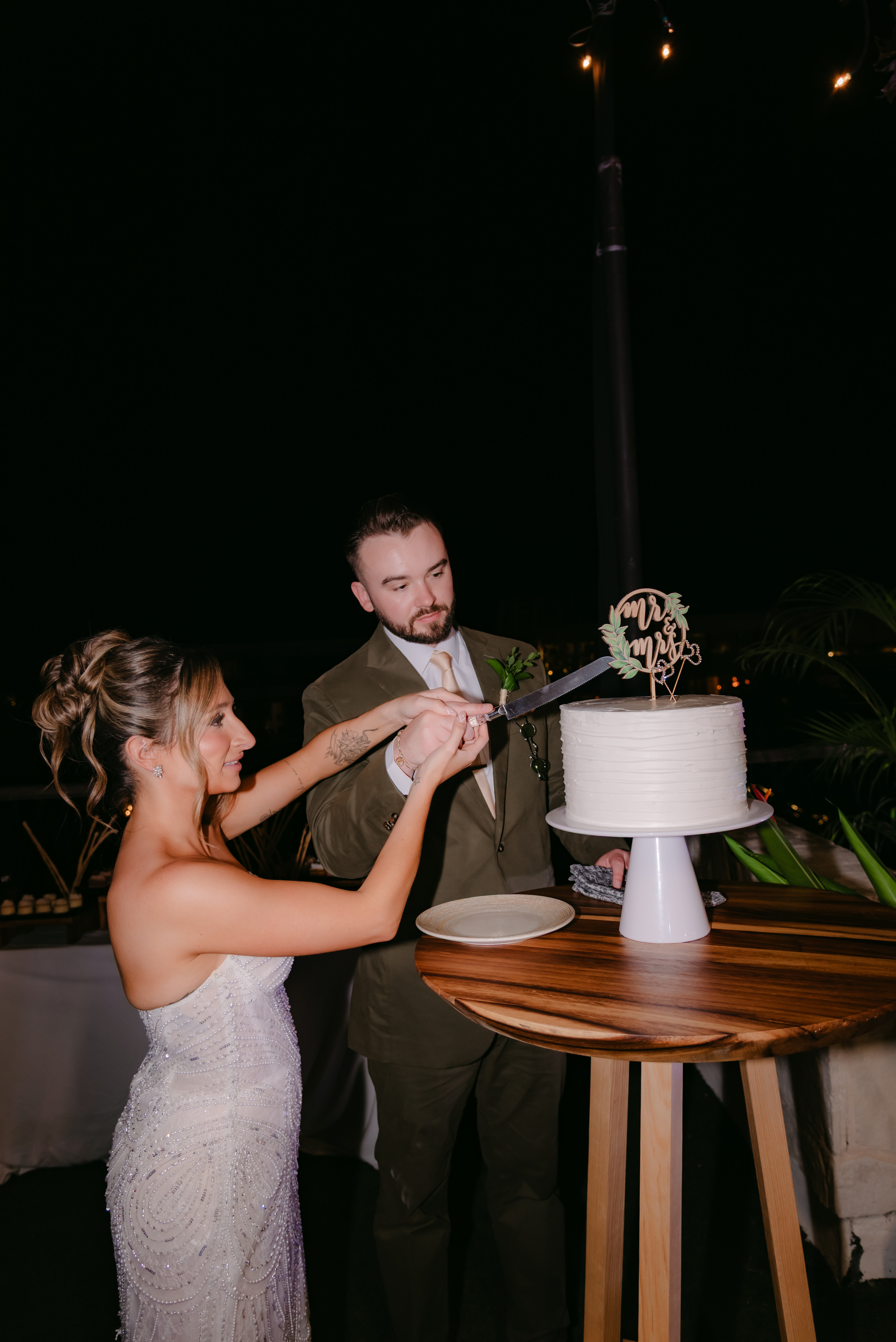 Shirley and William cut their white wedding cake together on a wooden table during a destination wedding.