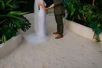 Shirley and William holding hands on a sandy path at their destination wedding, lush greenery all around.