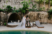Shirley and William at their destination wedding, posing by a poolside lounge with rocky, leafy scenery.