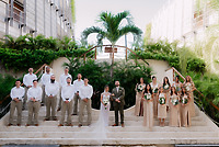 The Shirley and William destination wedding party poses outdoors, framed by lush greenery and palm trees.