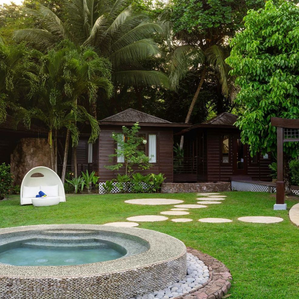 Round hot tub, stone path, white lounge chair, wooden cabin, and tropical trees—perfect for a destination wedding garden.