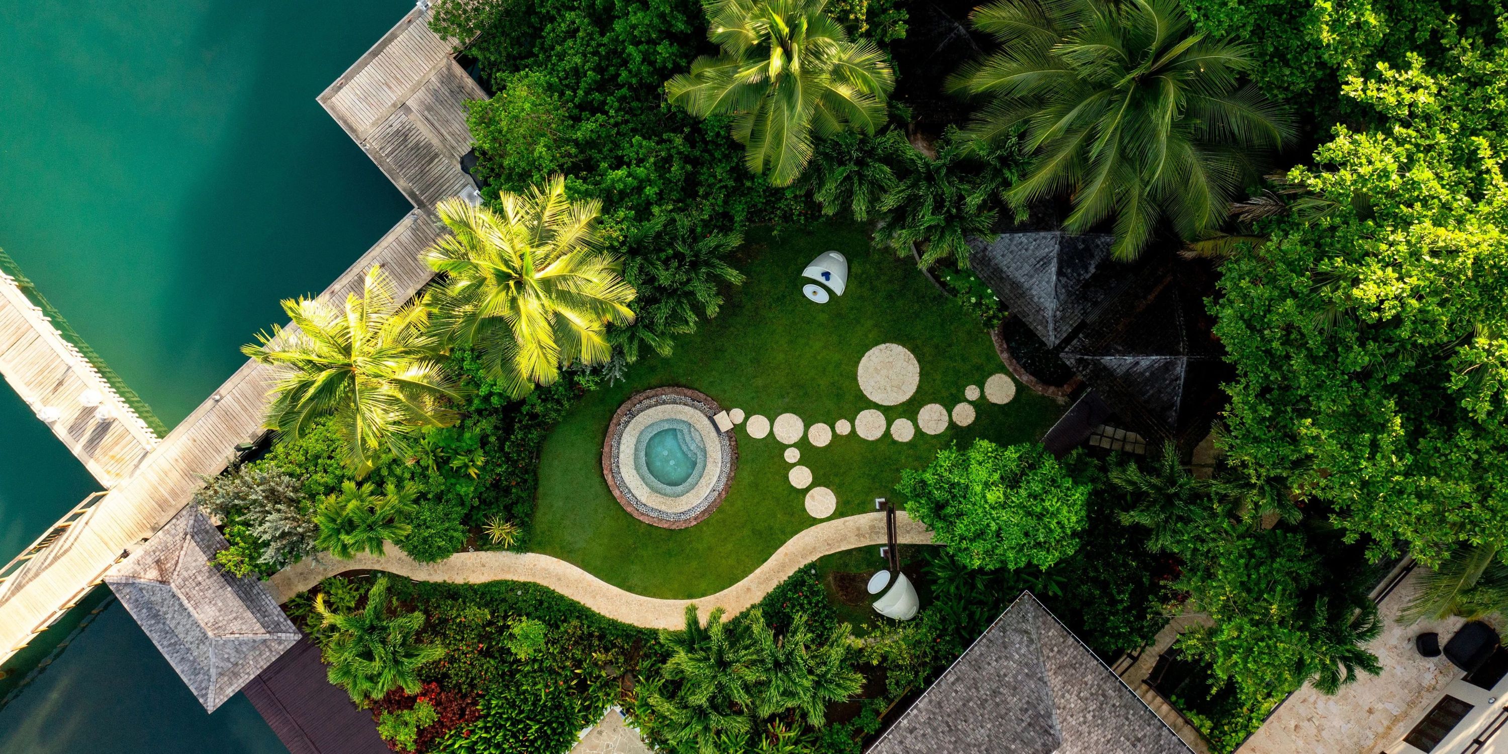 Aerial view of a lush garden set for a destination wedding, featuring a circular hot tub and stone path.