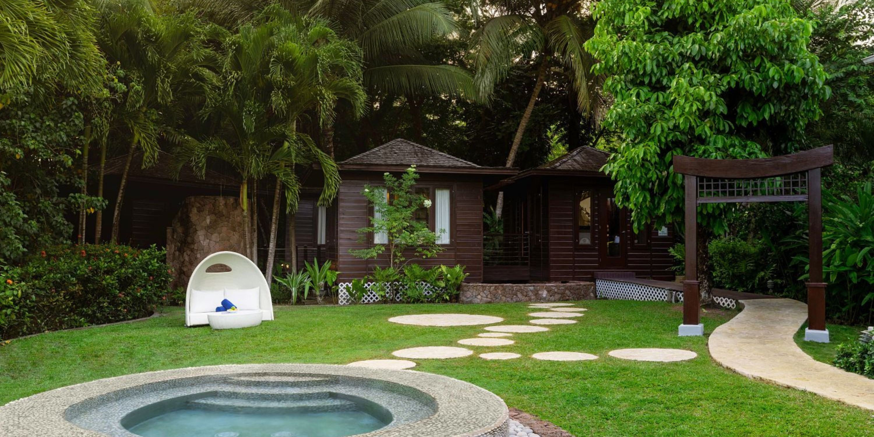 A wooden cottage perfect for a destination wedding, featuring a circular hot tub and lush tropical garden.