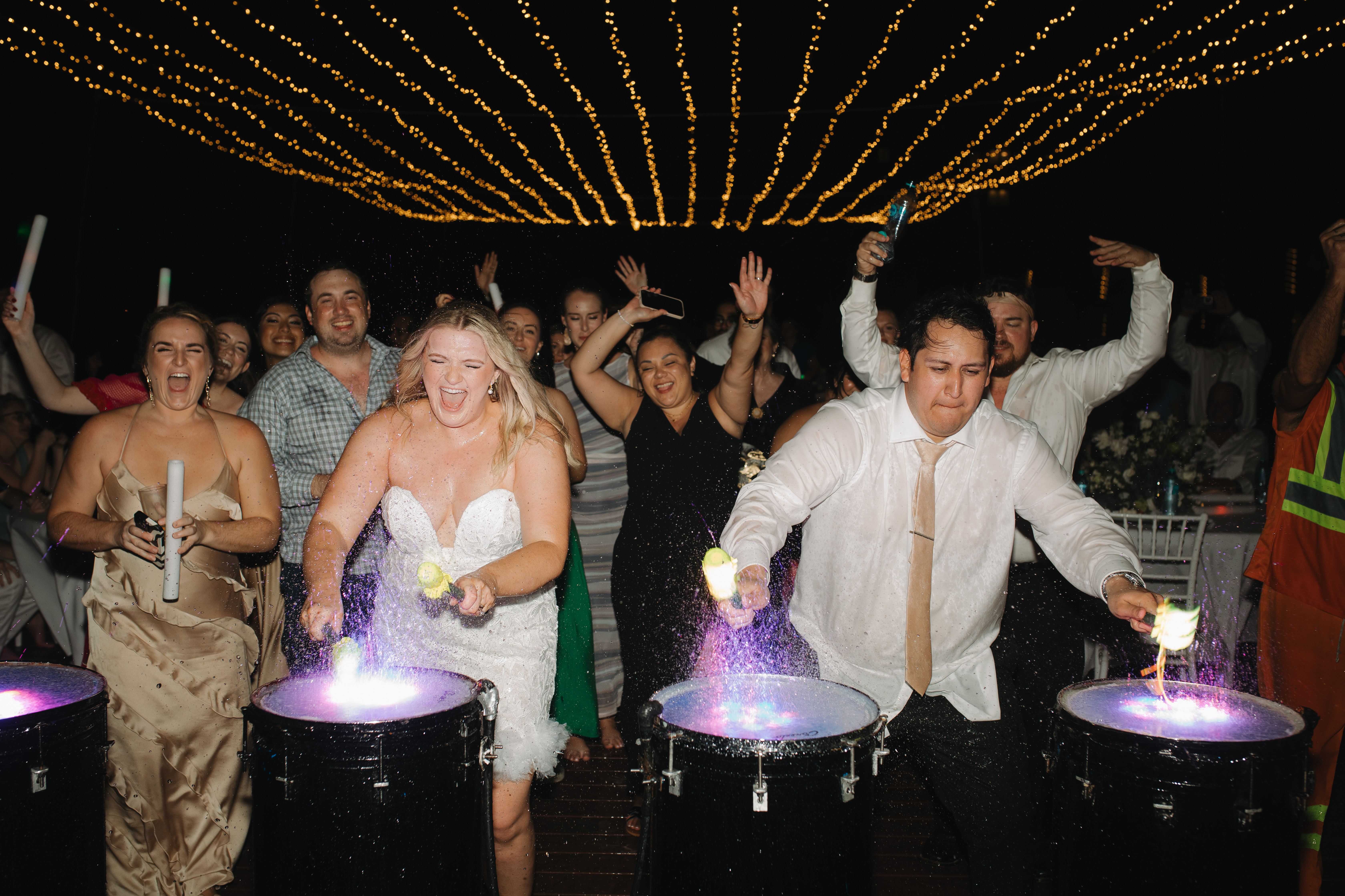 Madison and Robert play lit-up drums at their destination wedding as guests celebrate around them.