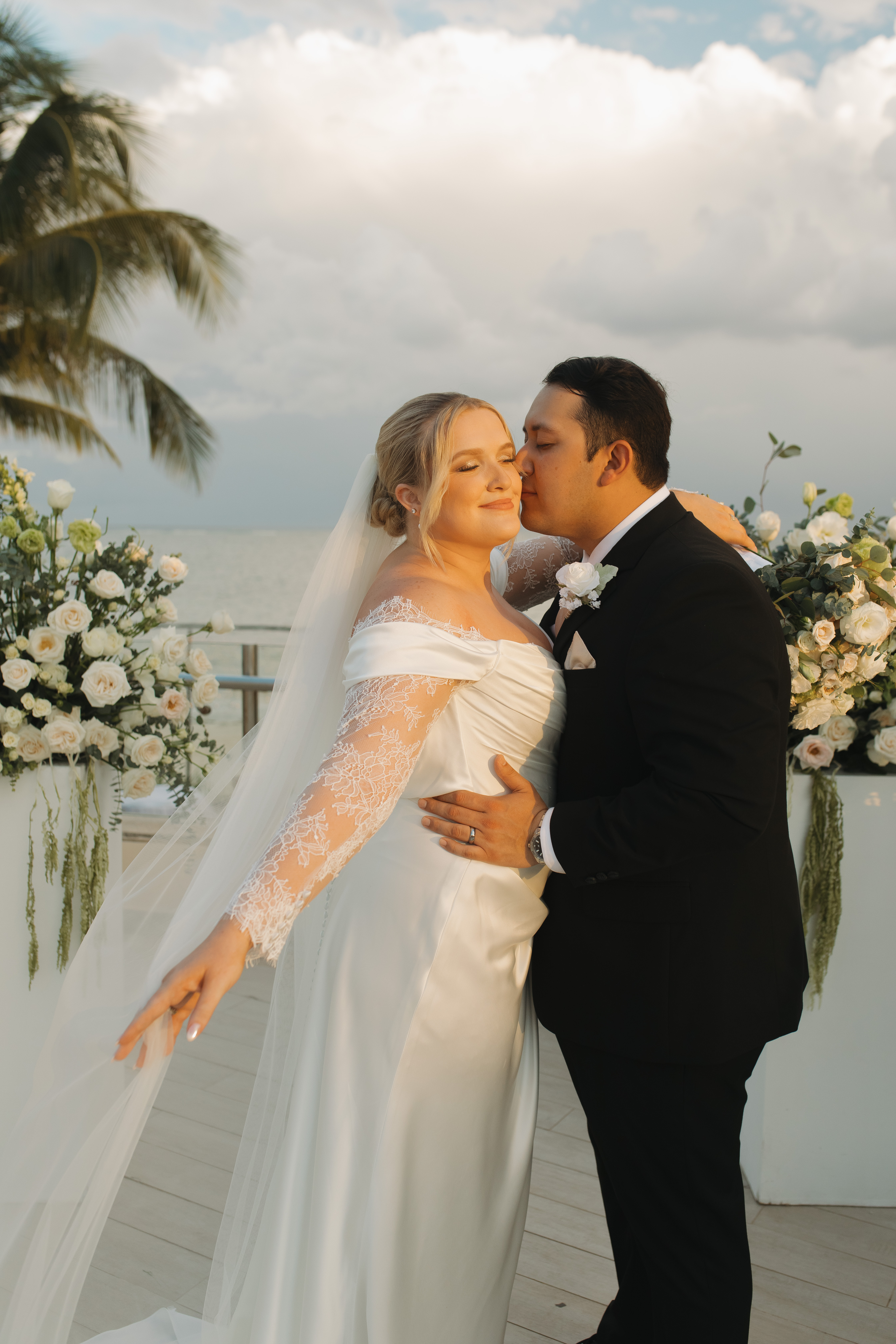 Madison and Robert embrace on a terrace at their destination wedding, surrounded by floral arrangements.