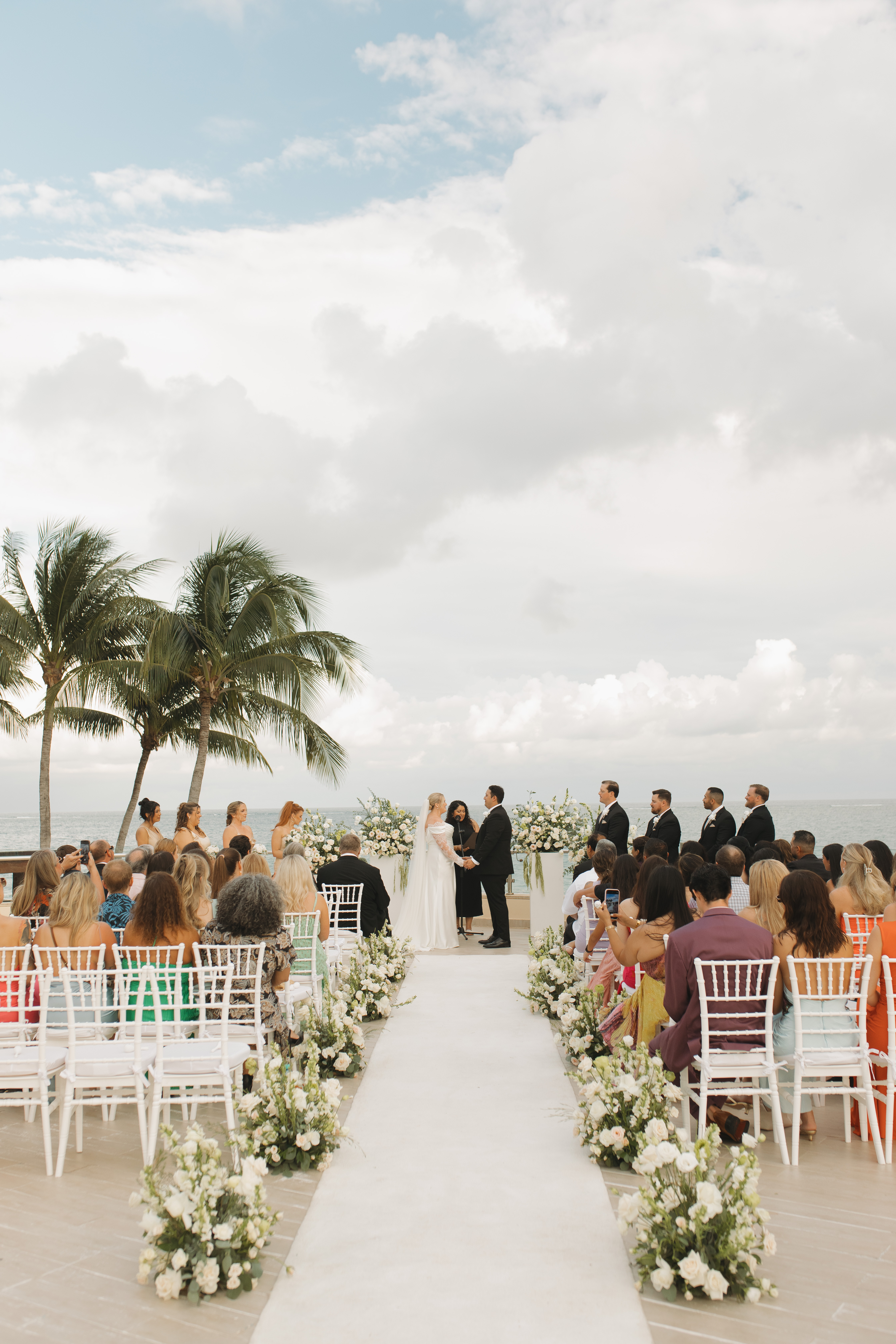 Madison and Robert's destination wedding by the ocean, guests seated with palm trees in the background.