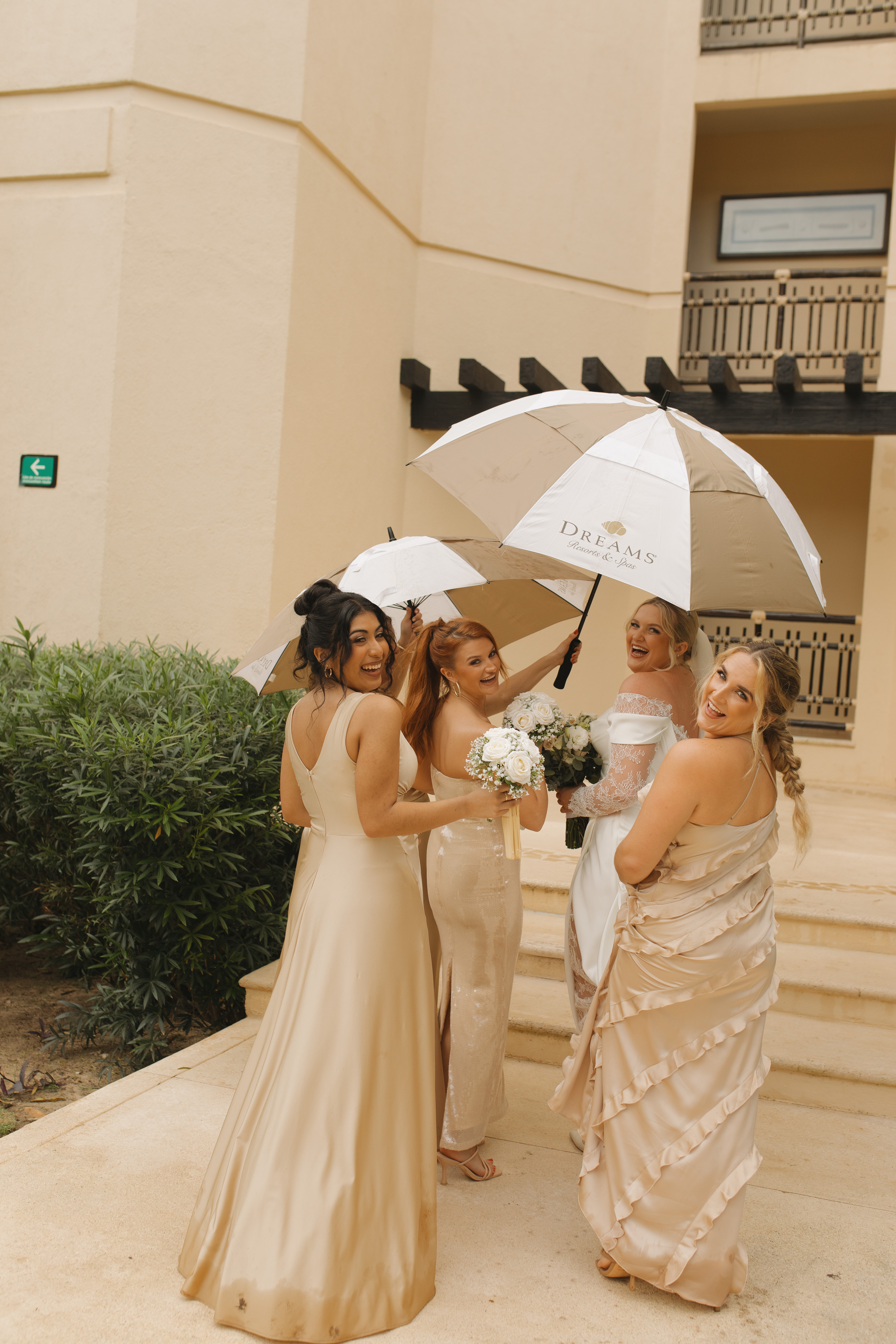 At a destination wedding, four women in formal dresses with Madison and Robert, holding umbrellas and flowers.