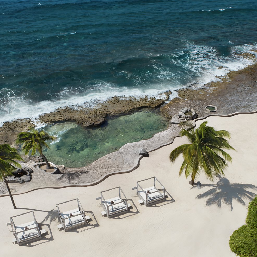 Four cabanas on white sand near palm trees, perfect for a destination wedding by rocky ocean shore.