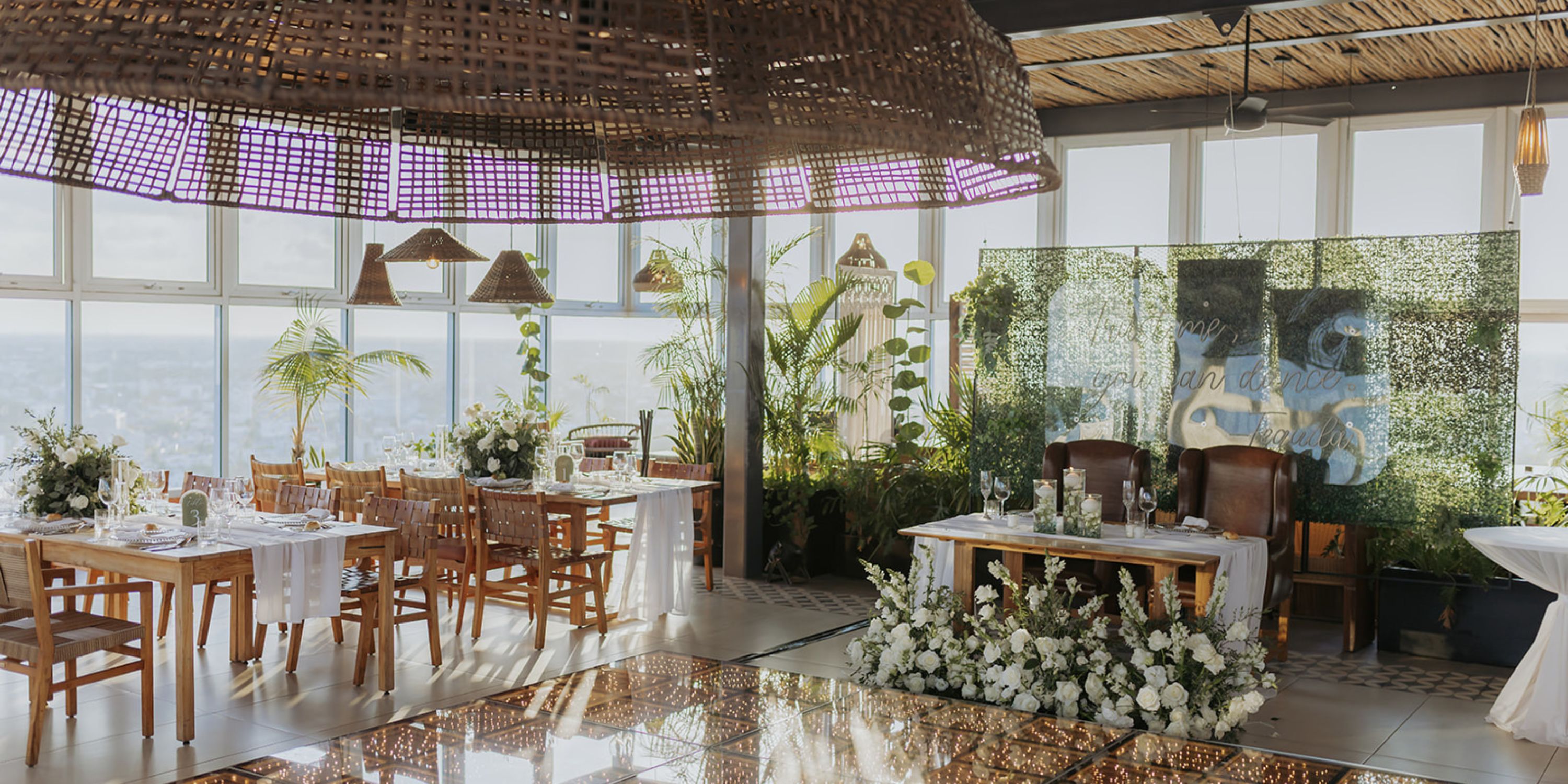 Chic destination wedding venue featuring wooden tables, lush floral arrangements, and a greenery backdrop.