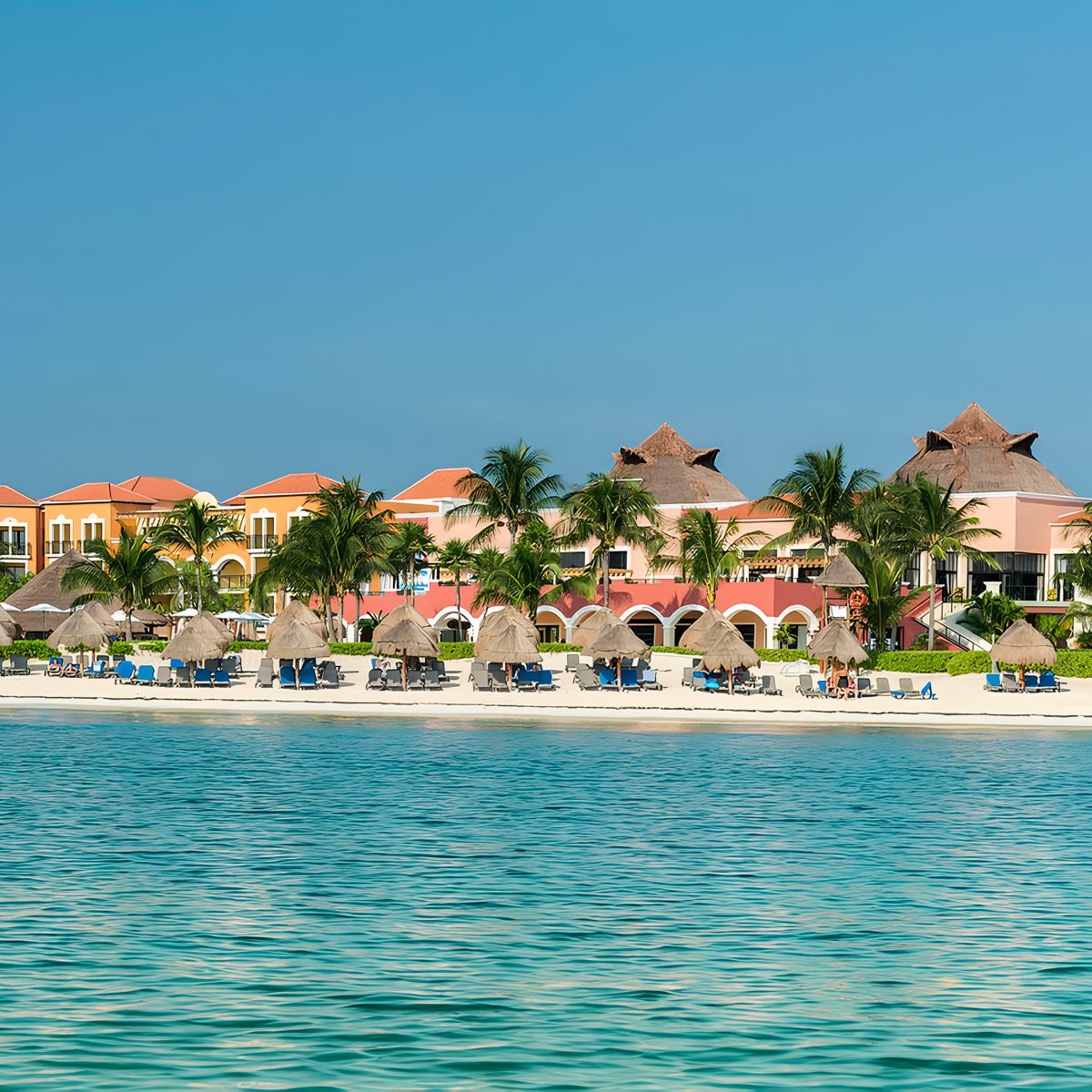 Ocean Coral and Turquesa resort, perfect for a destination wedding, with straw umbrellas and vivid buildings.