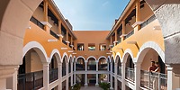 Ocean Coral and Turquesa: Yellow and white arched courtyard with balconies, ideal for destination wedding; two people visible on right.