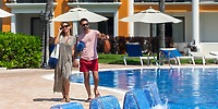 A couple, possibly celebrating a destination wedding, walks hand-in-hand by the pool at Ocean Coral and Turquesa.