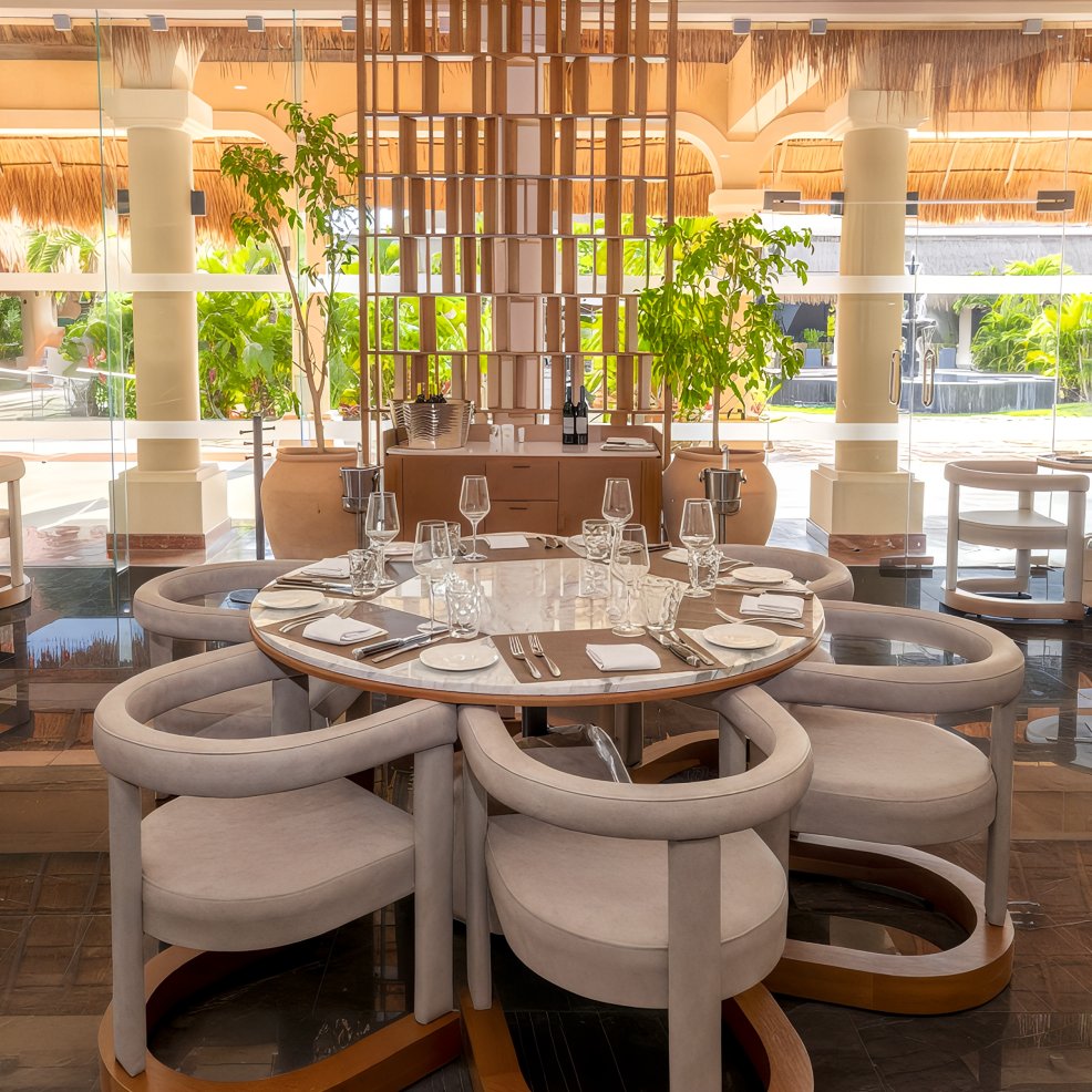 Round dining table set for six with modern chairs in a bright, upscale destination wedding venue.