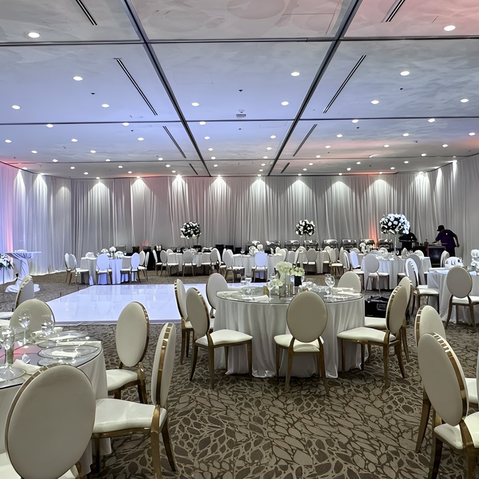 Spacious banquet hall with round tables, white chairs, and floral centerpieces set for a destination wedding.