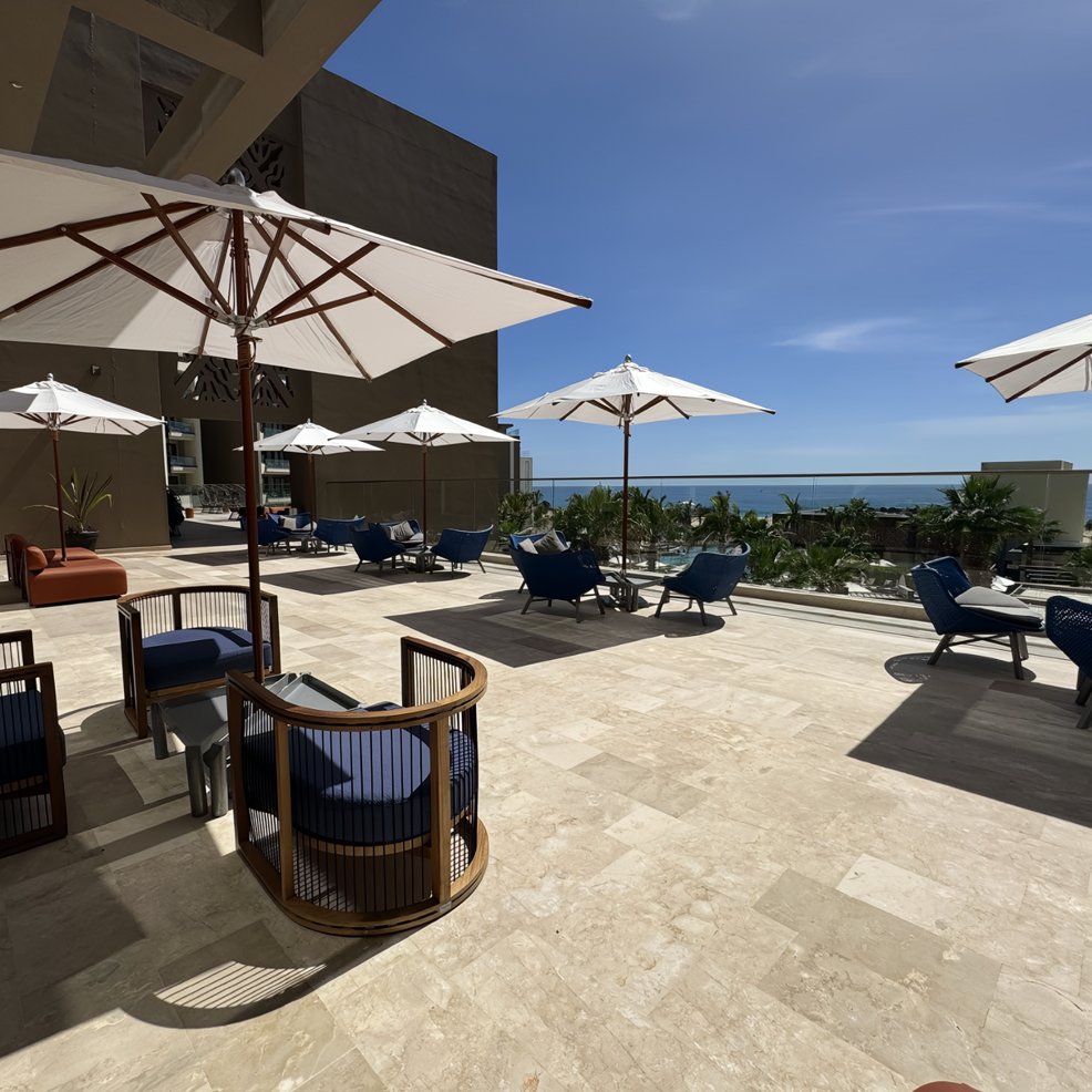 Outdoor patio set for a destination wedding, with blue cushioned chairs, tables, and white umbrellas by the ocean.