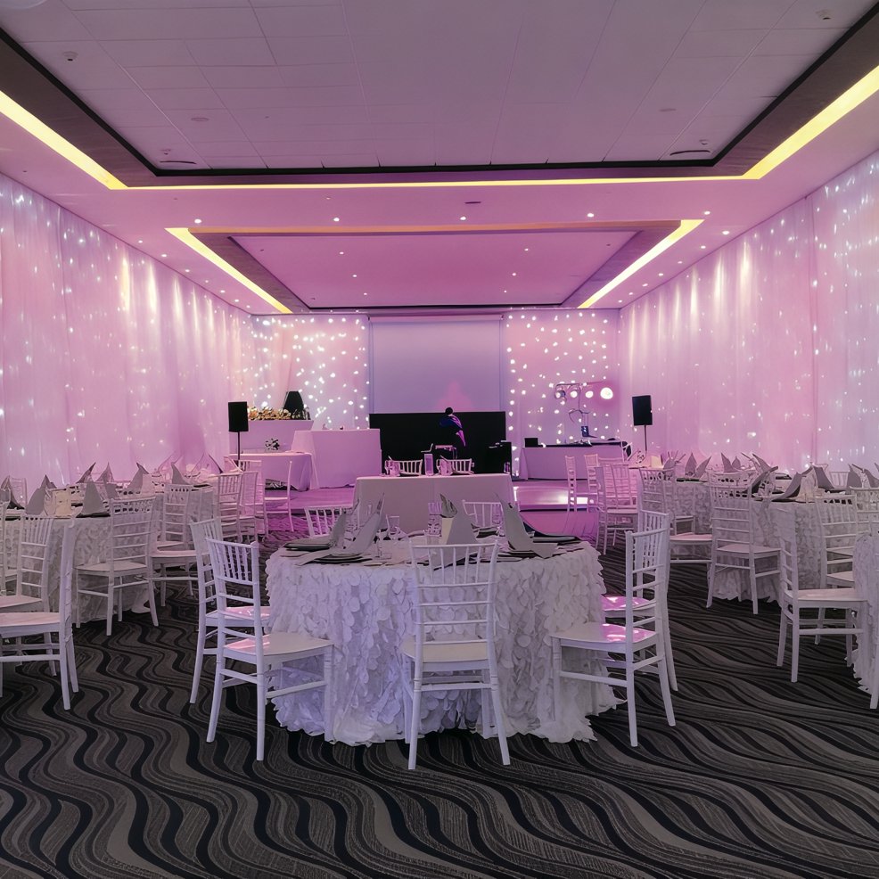 Elegant wedding banquet hall with round tables, white chairs, and soft pink lighting for a destination wedding.