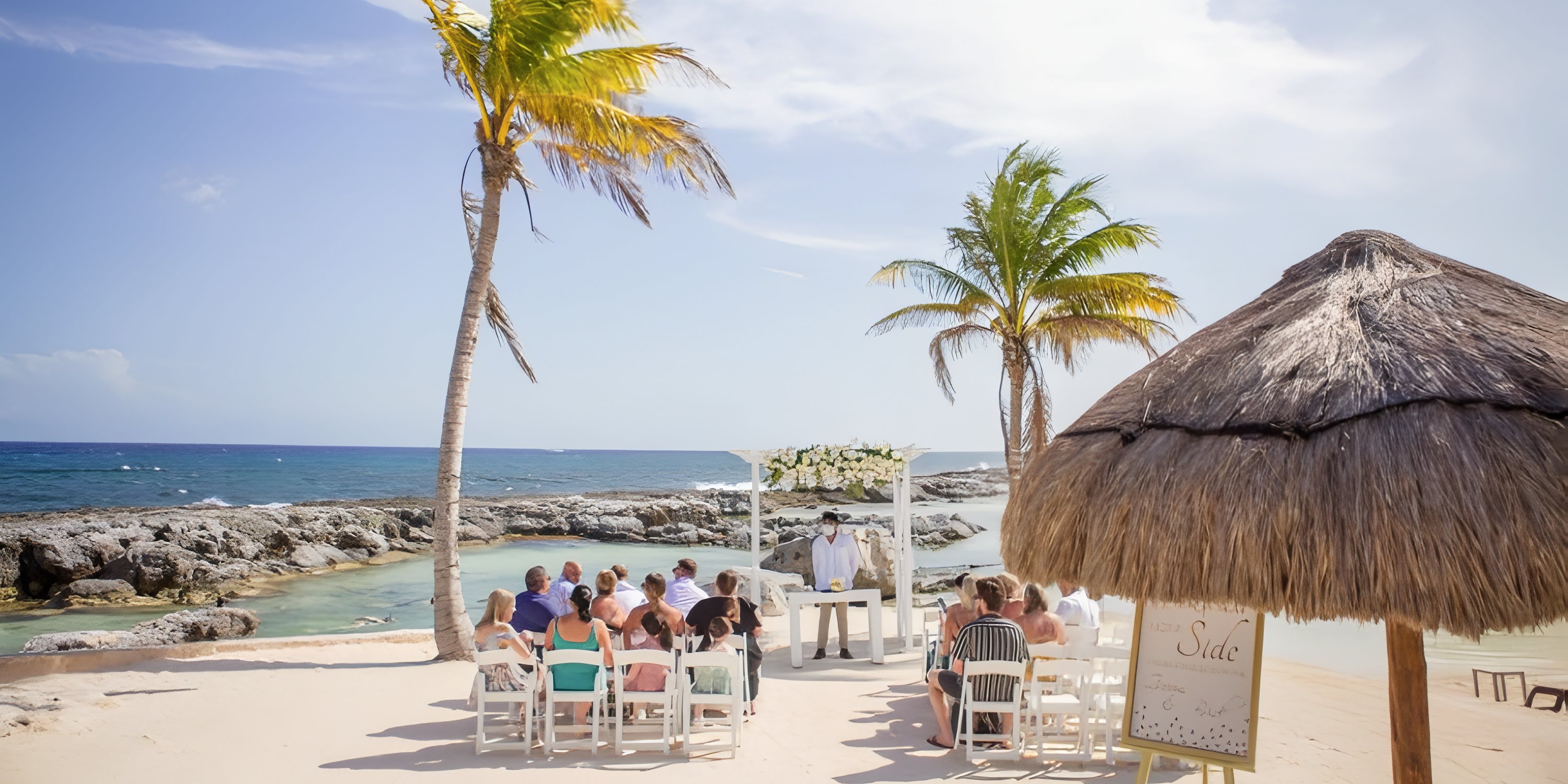 Intimate destination wedding by the ocean, guests seated under palm trees for the ceremony.