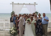 Stephanie and Connor's destination wedding party smiles with drinks by the beachside wedding altar.