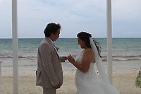 Stephanie and Connor exchange rings during their destination wedding on a beach with the ocean behind them.