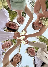 Six people in wedding attire toast drinks above, viewed from below at Stephanie and Connor&rsquo;s destination wedding.