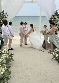 Stephanie and Connor exchange vows at their destination wedding on the beach, surrounded by flowers and friends.