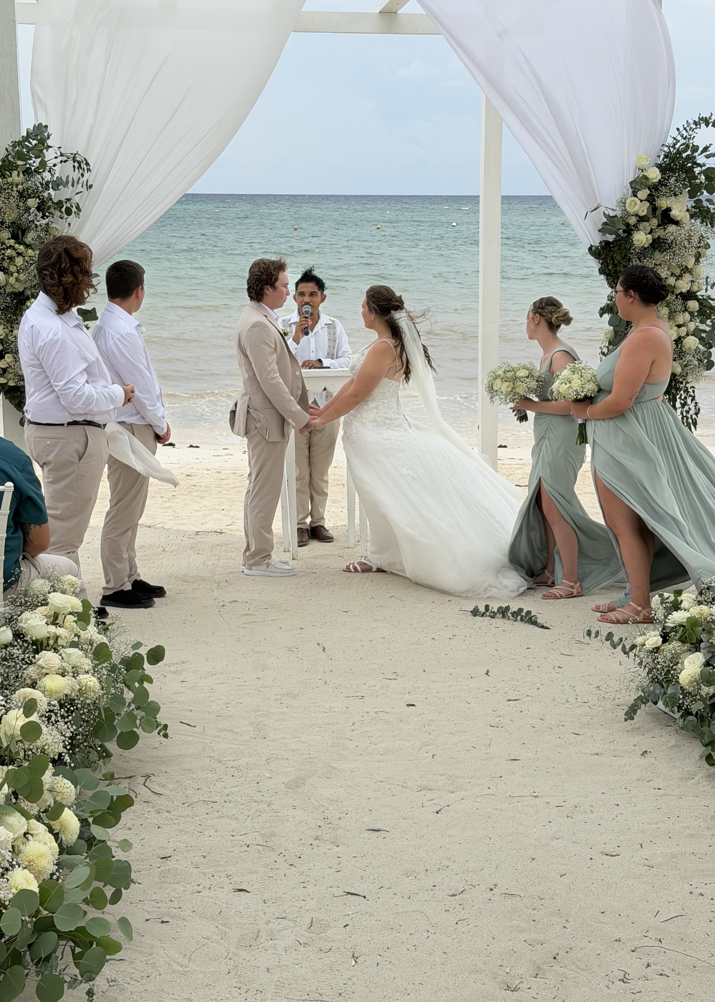 Stephanie and Connor exchange vows at their destination wedding on the beach, surrounded by flowers and friends.