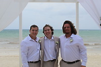 Three men pose in Stephanie and Connor wedding shirts on a beach, ocean behind them at a destination wedding.