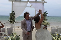 Stephanie and Connor share a dance at their destination wedding under a flower-decorated white pergola on the beach.