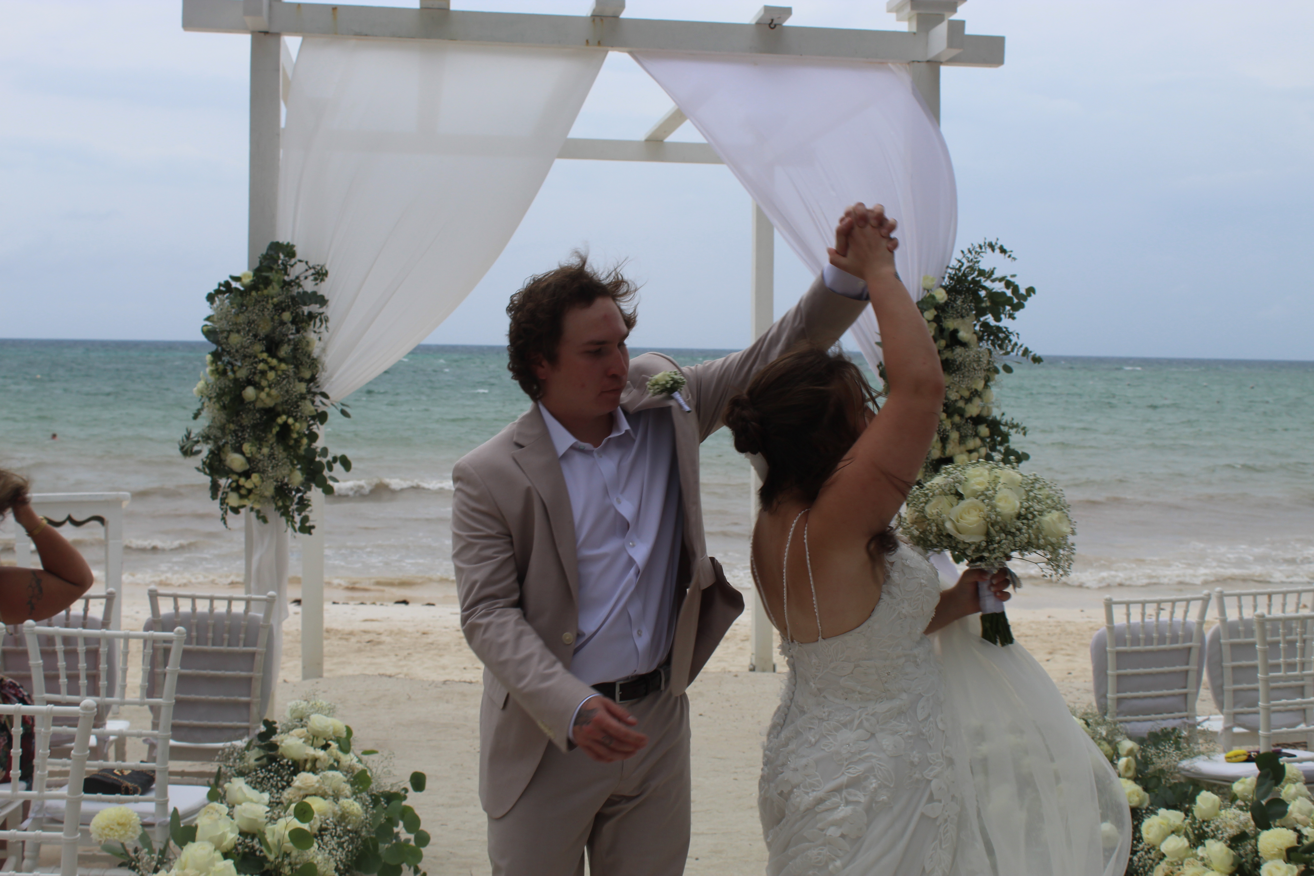 Stephanie and Connor share a dance at their destination wedding under a flower-decorated white pergola on the beach.