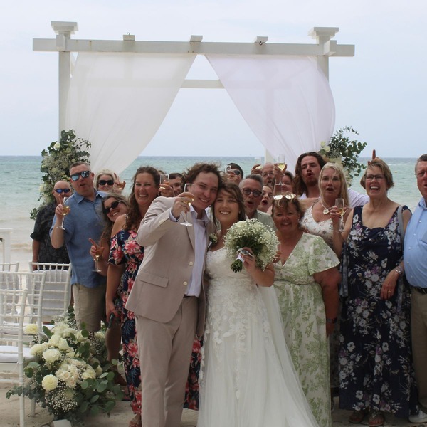 Stephanie and Connor celebrate with guests at a destination wedding on the beach, raising champagne glasses.