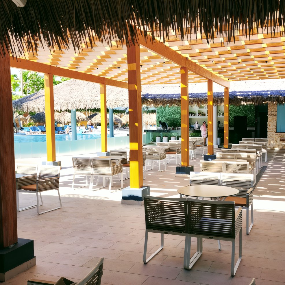 Outdoor patio with tables and chairs under a thatched roof, perfect for a destination wedding by the pool.