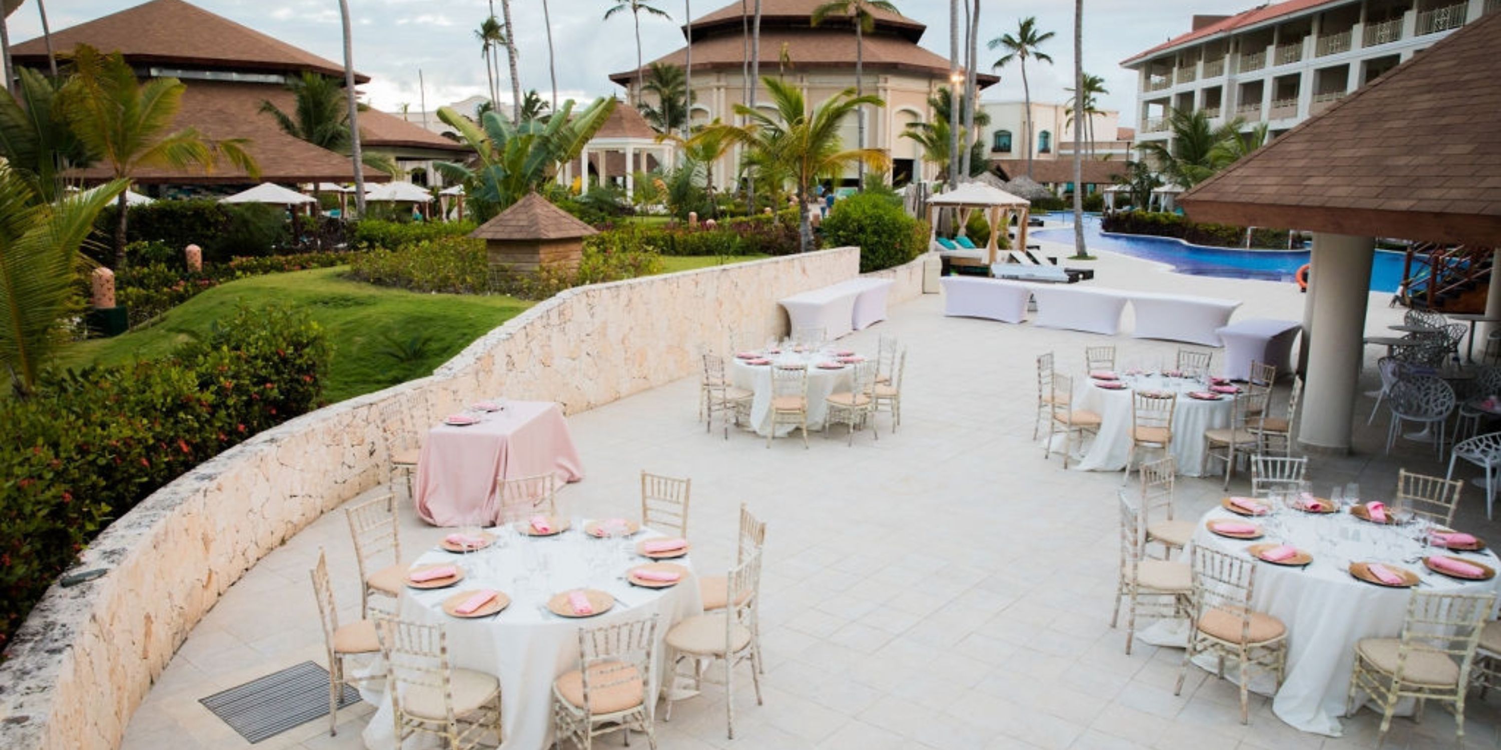 Outdoor patio with round tables elegantly arranged for a destination wedding near a resort pool.