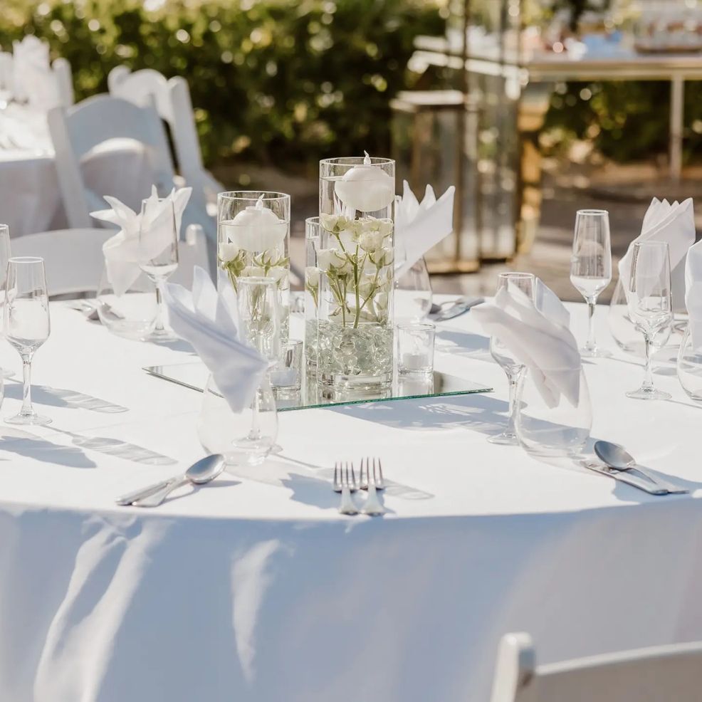 Round table set for a destination wedding with white linens, glassware, and a floral centerpiece.
