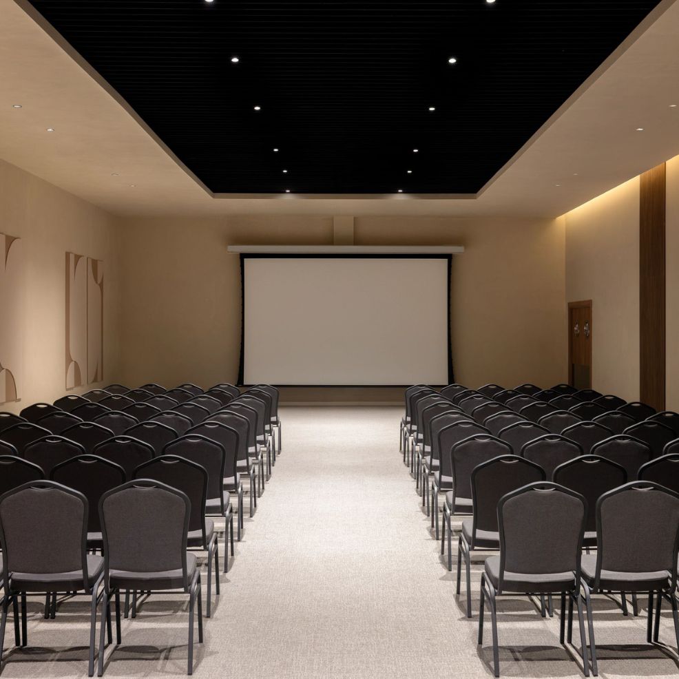 Rows of black chairs face a blank screen in a modern room, set up for a destination wedding event.