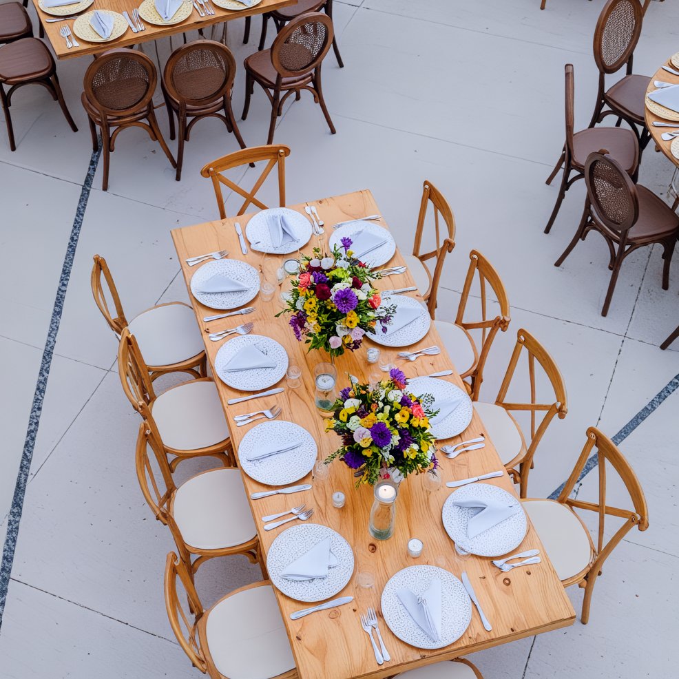 An overhead view of a wooden table set for a destination wedding, with plates, napkins, and flowers.