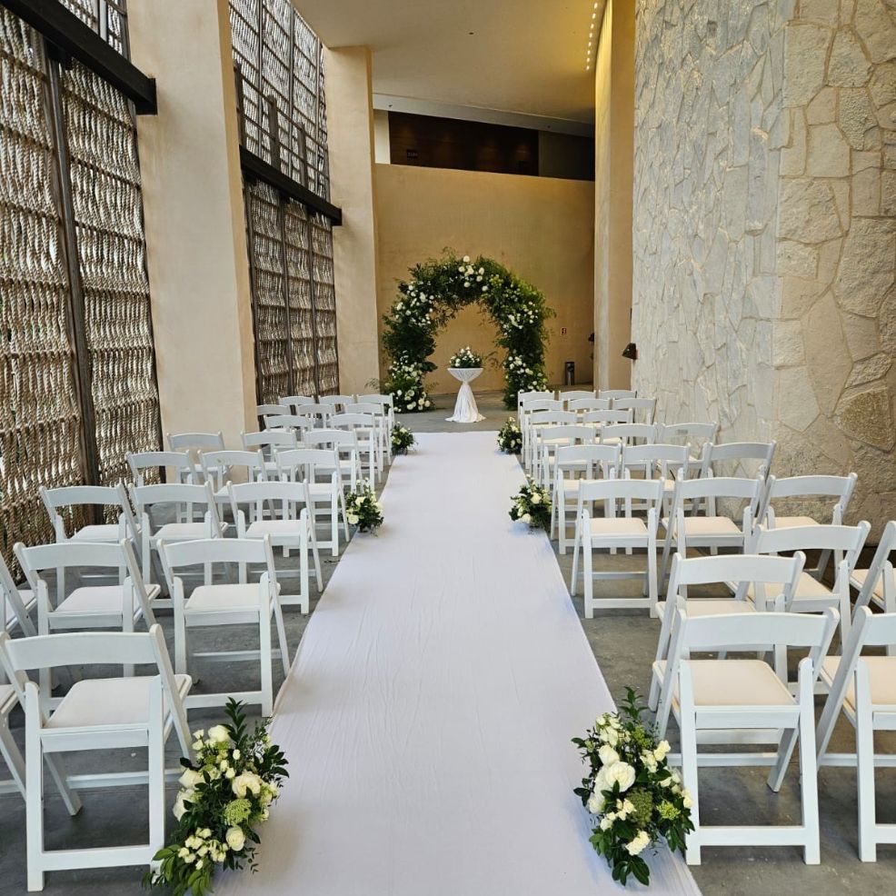 Destination wedding ceremony setup with white chairs, a white aisle runner, and elegant floral displays.
