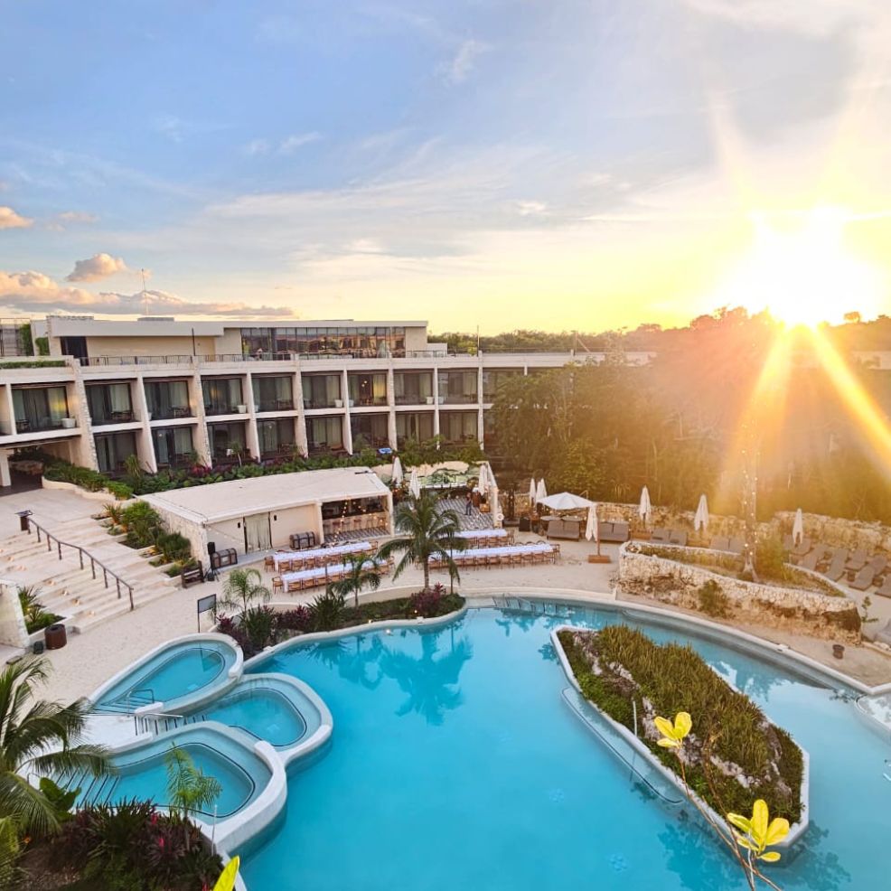 Resort pool with lounge chairs and palm trees at sunset, perfect for a destination wedding, hotel behind.