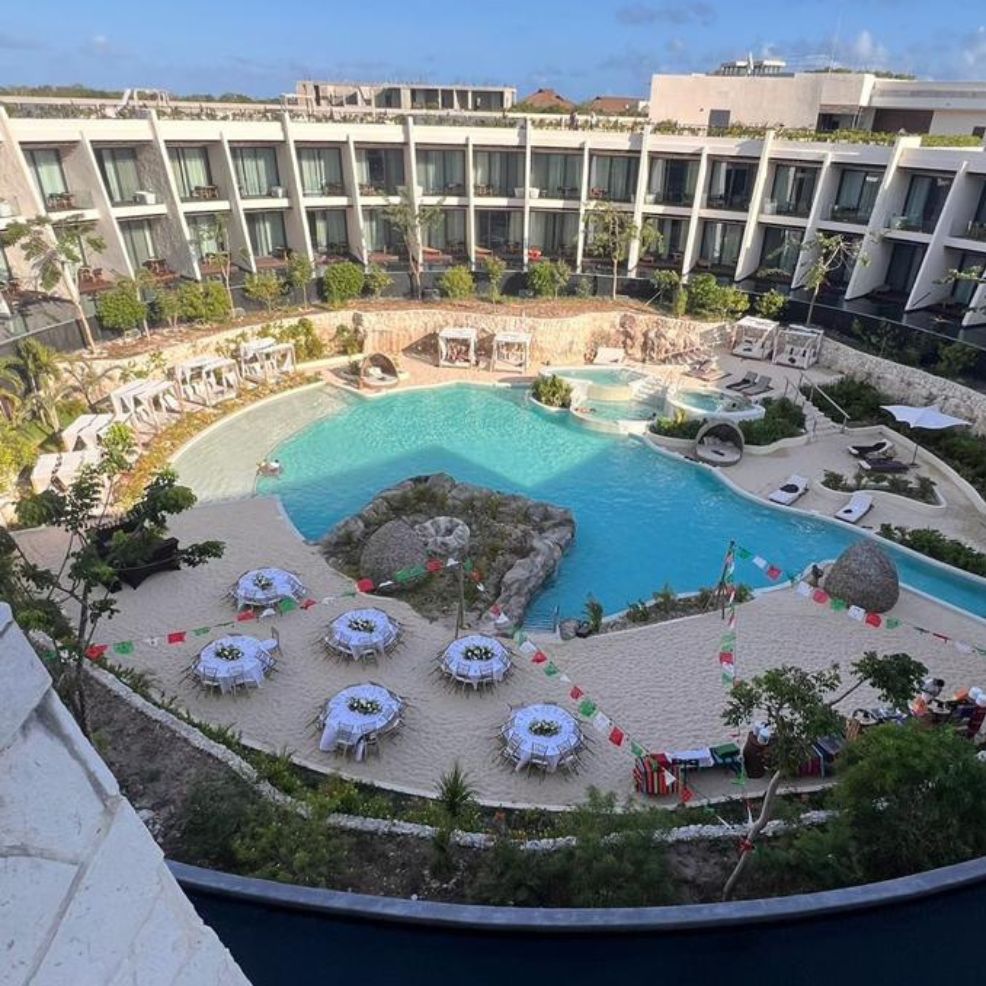 A hotel courtyard set for a destination wedding with a large pool, sandy tables, and festive decor.