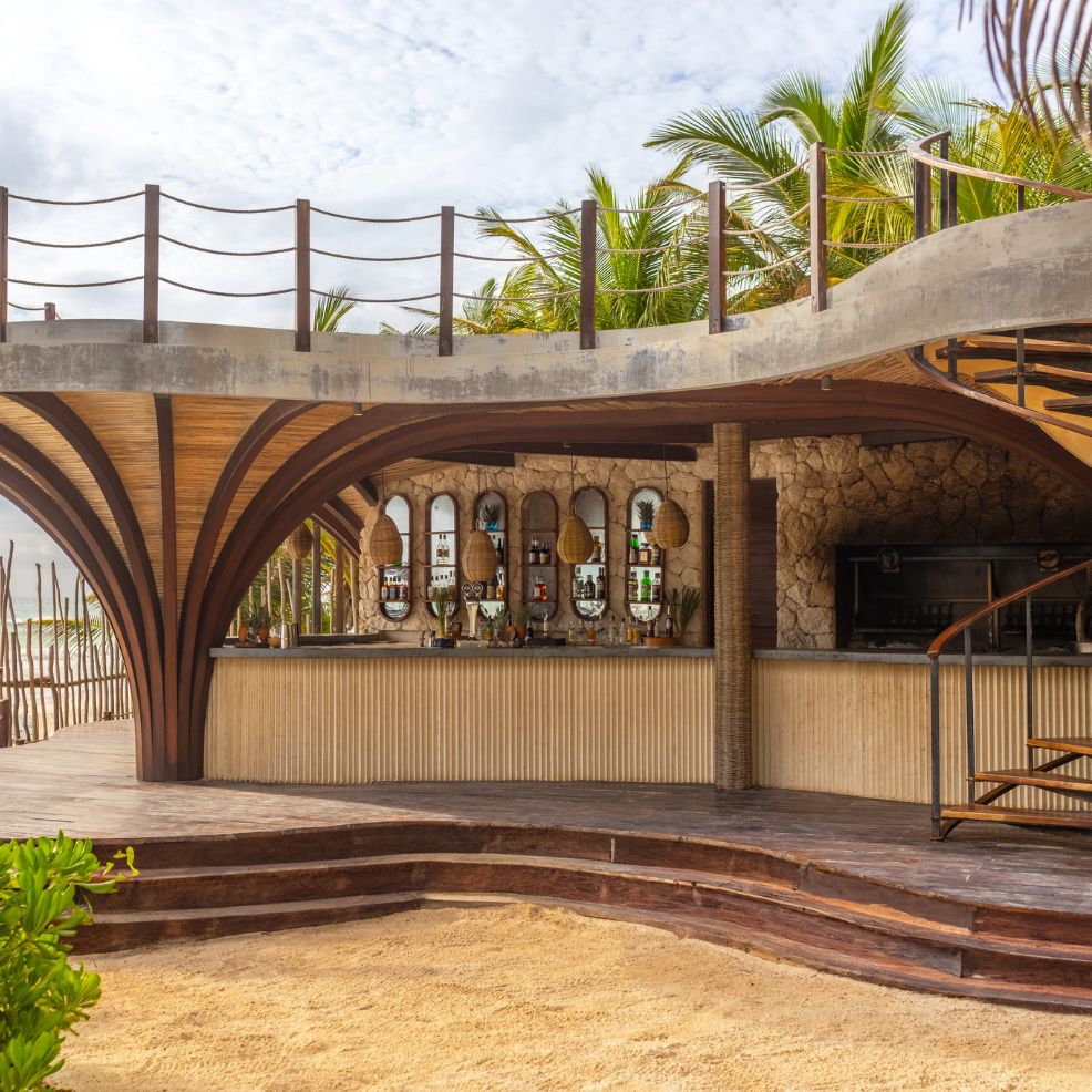 Scenic beach bar with wooden beams, stone walls, arches, and palm trees&mdash;ideal for a destination wedding.