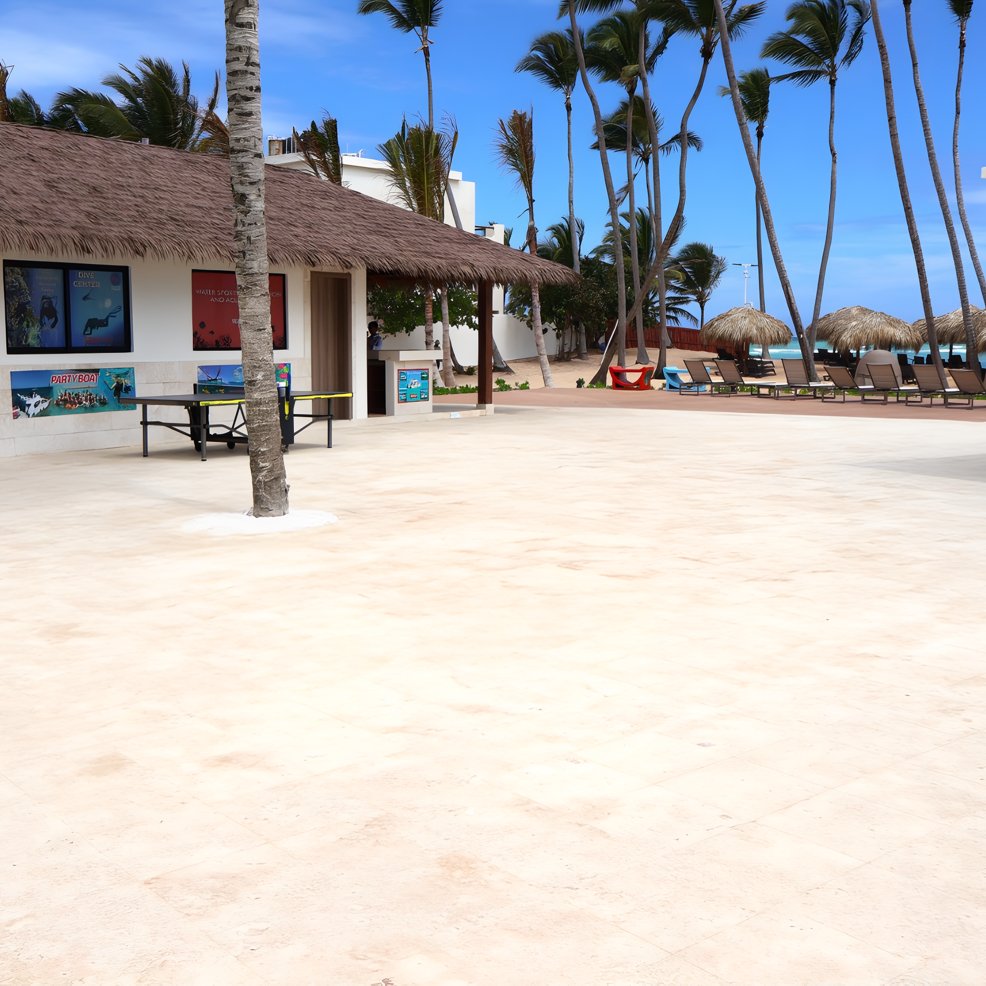 A destination wedding patio with palm trees, lounge chairs, and a thatched-roof venue under blue skies.