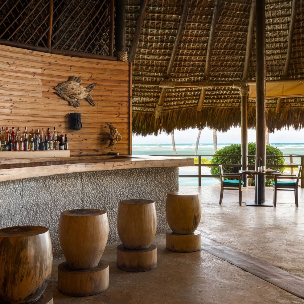 Outdoor bar with wooden stools, thatched roof, and ocean view—ideal for a destination wedding.