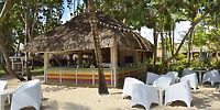 A thatched-roof bar at Catalonia Bayahibe, perfect for a destination wedding, with white chairs on sand.